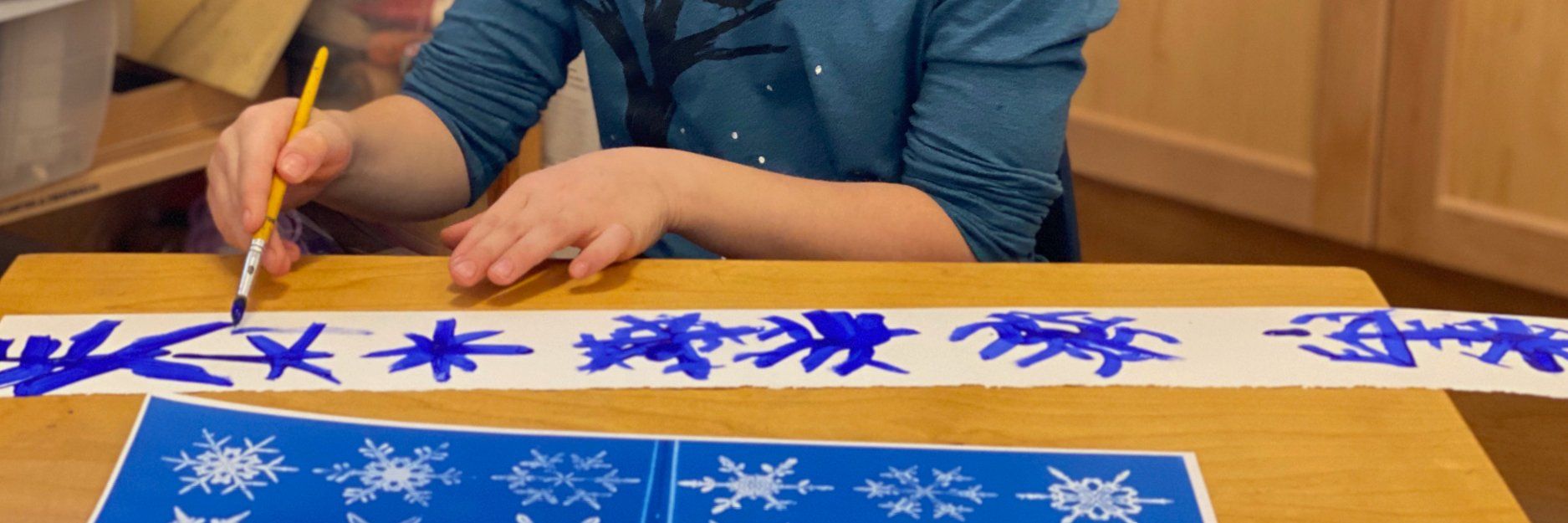 Child at table looking at and painting images of snowflakes