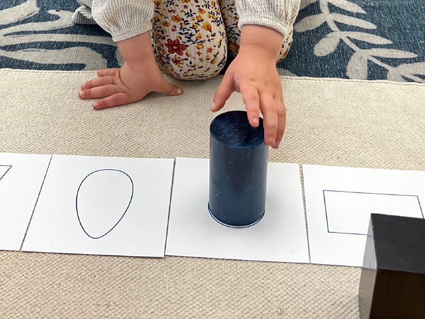 image of a preschool aged child kneeling on a carpet on the floor working with 3-D shapes and cards