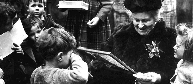 black and white photo of Maria Montessori surrounded by young children