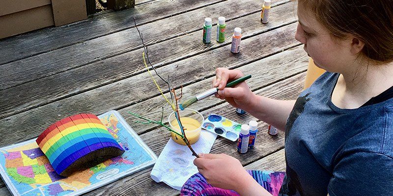 eighth grade student sitting on a deck with paints and other art supplies