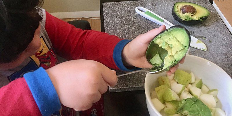 Young child scooping avocado out of skin
