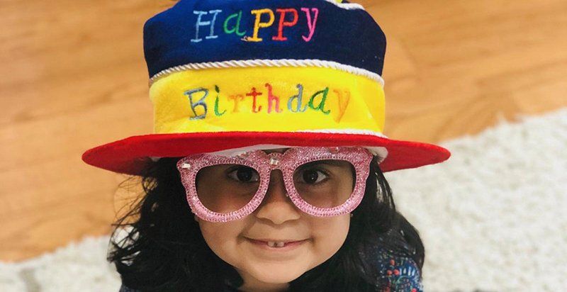 smiling preschool aged child wearing a brightly colored hat that reads Happy Birthday