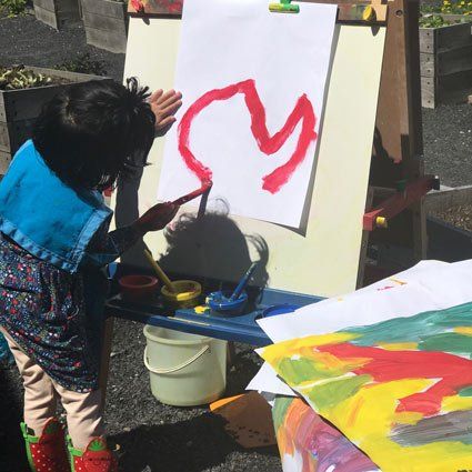 Children's House (preschool) child painting outdoors at easel
