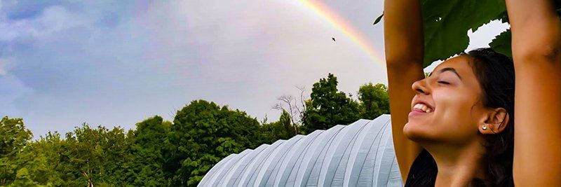Young woman in front of a greenhouse, rainbow in sky