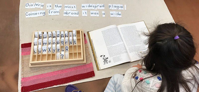 Child with book and alphabet tiles, making a sentence
