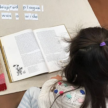 child with book and alphabet tiles, making sentences.