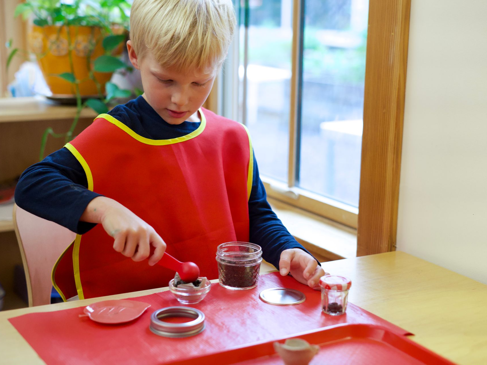Image of a preschool aged child wearing an apron standing at a table with several containers of soil