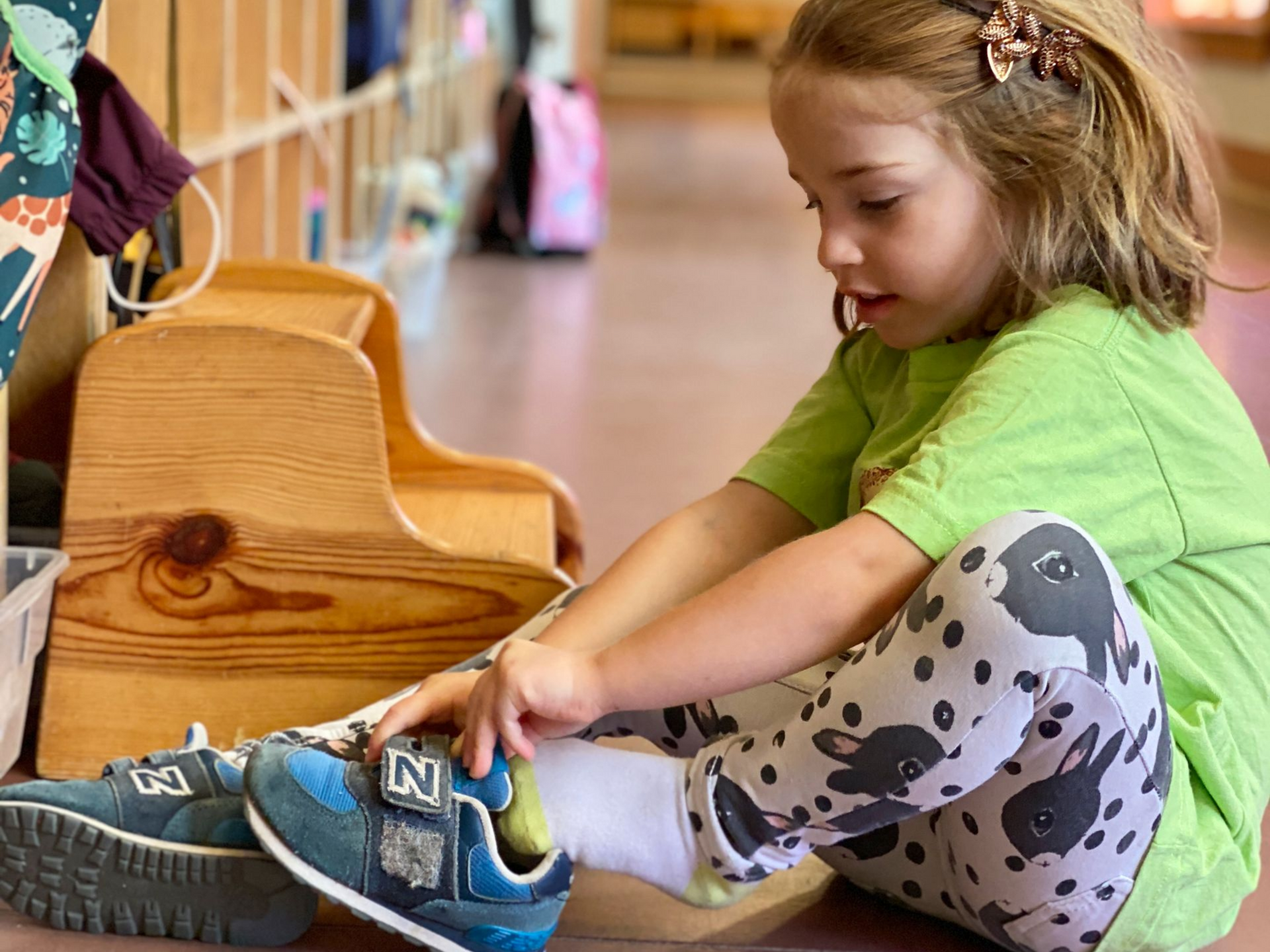 Image of a preschool child sitting on the floor putting on a sneaker