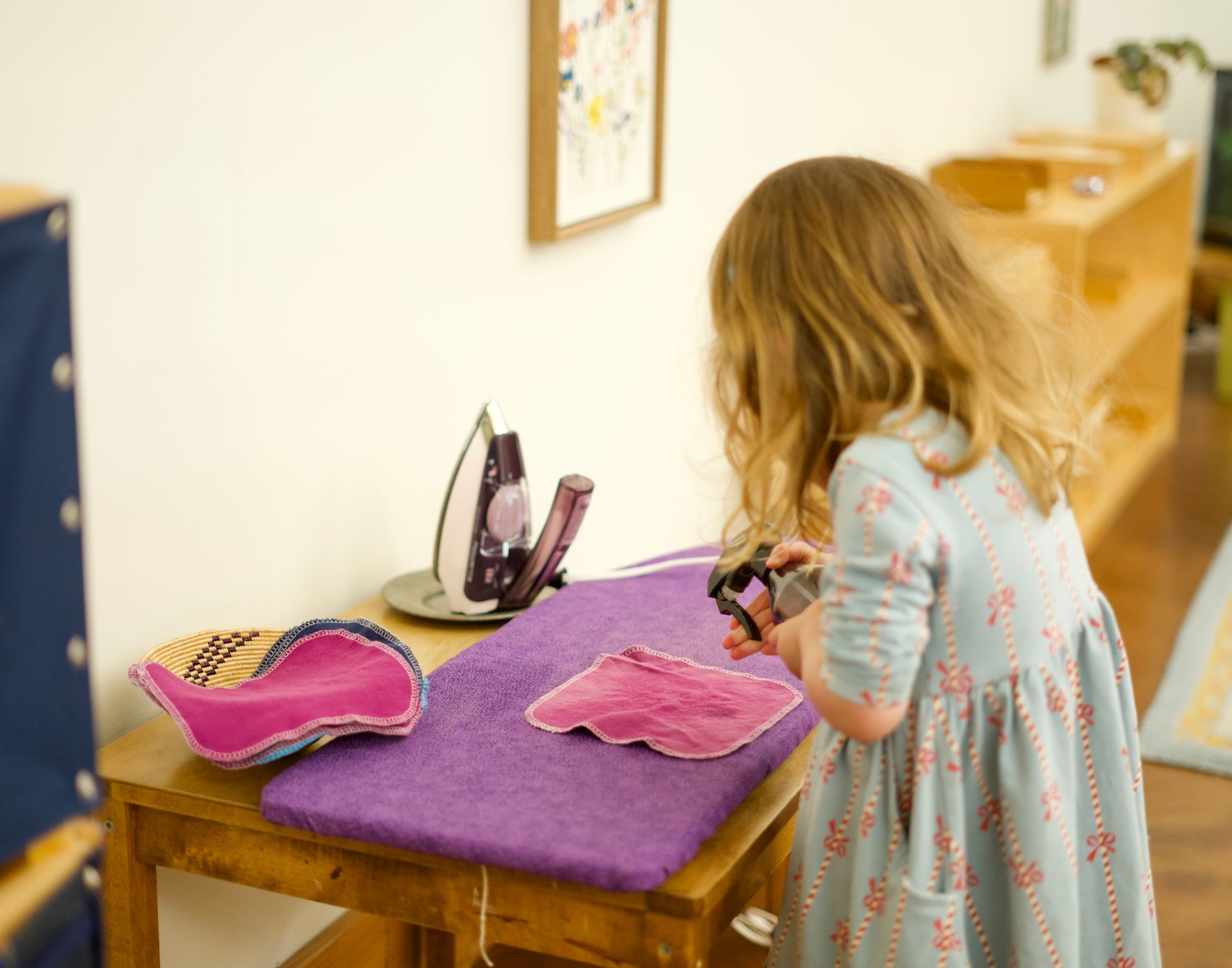 Image of a preschool aged girl standing in front of an ironing board with a spray bottle and fabric