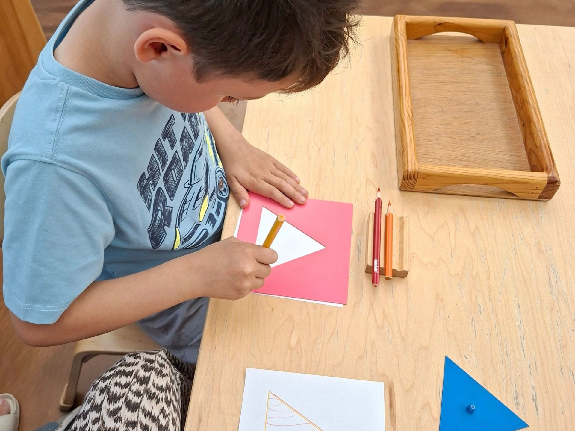 Image of a preschool aged child holding a pencil, sitting at a small table with a flat metal square 