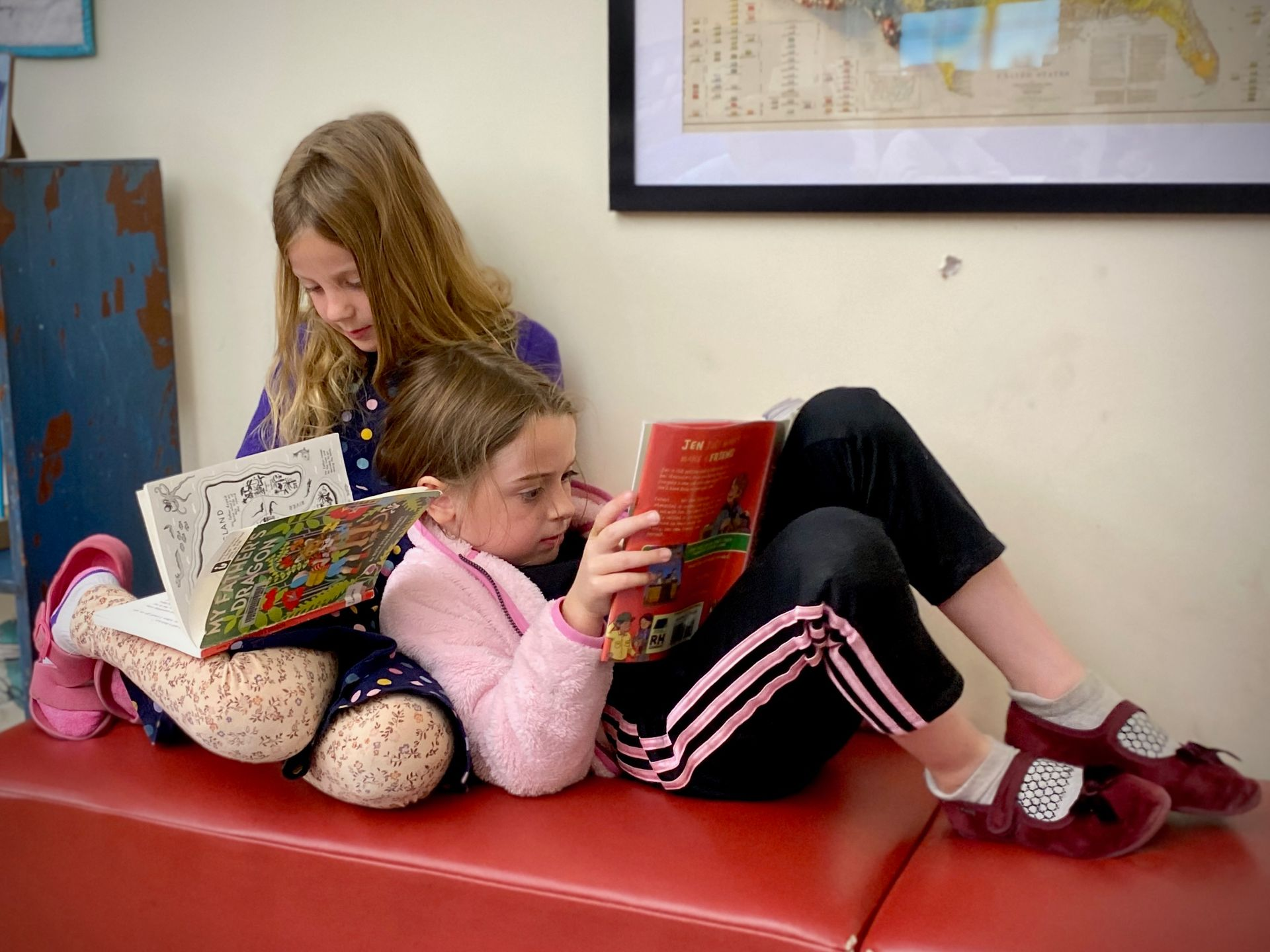 image of two elementary aged girls sitting on a bench, leaning on each other while reading