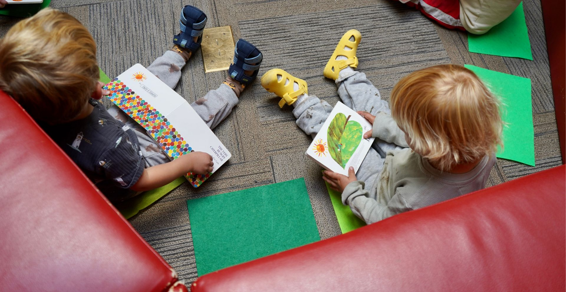 Looking over the shoulders of two toddlers sitting on the floor reading books