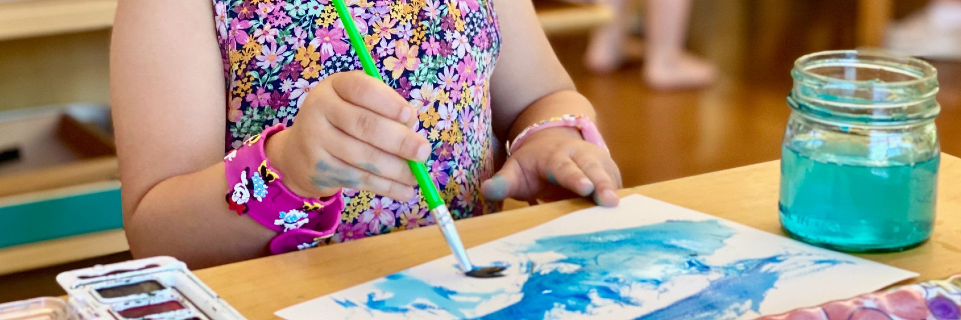 Close up cropped image of a child's arms using watercolor paints at a table
