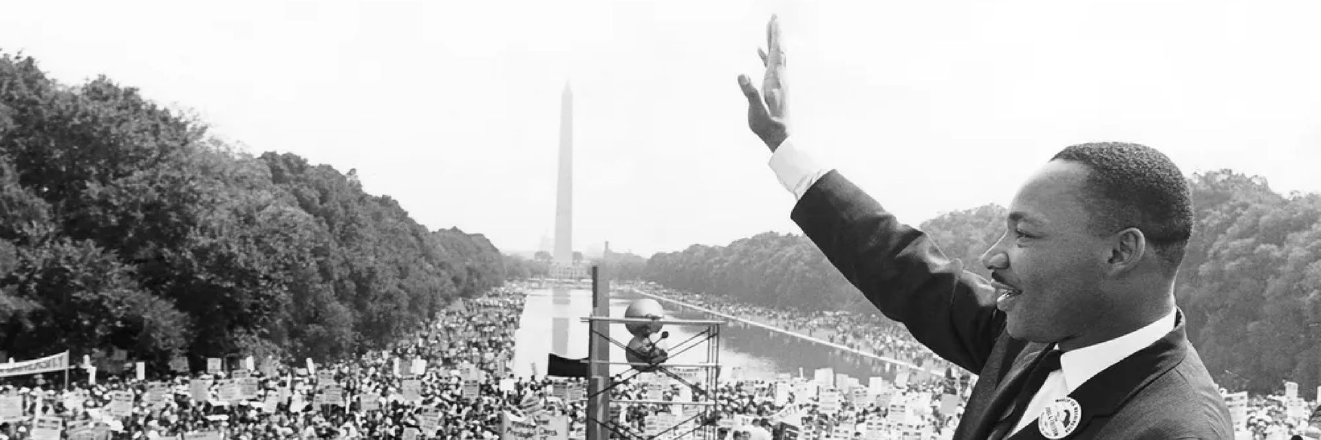 black and white image of Dr. Martin Luther King Jr. waving to the crowd gathered around the reflecting pool in Washington DC