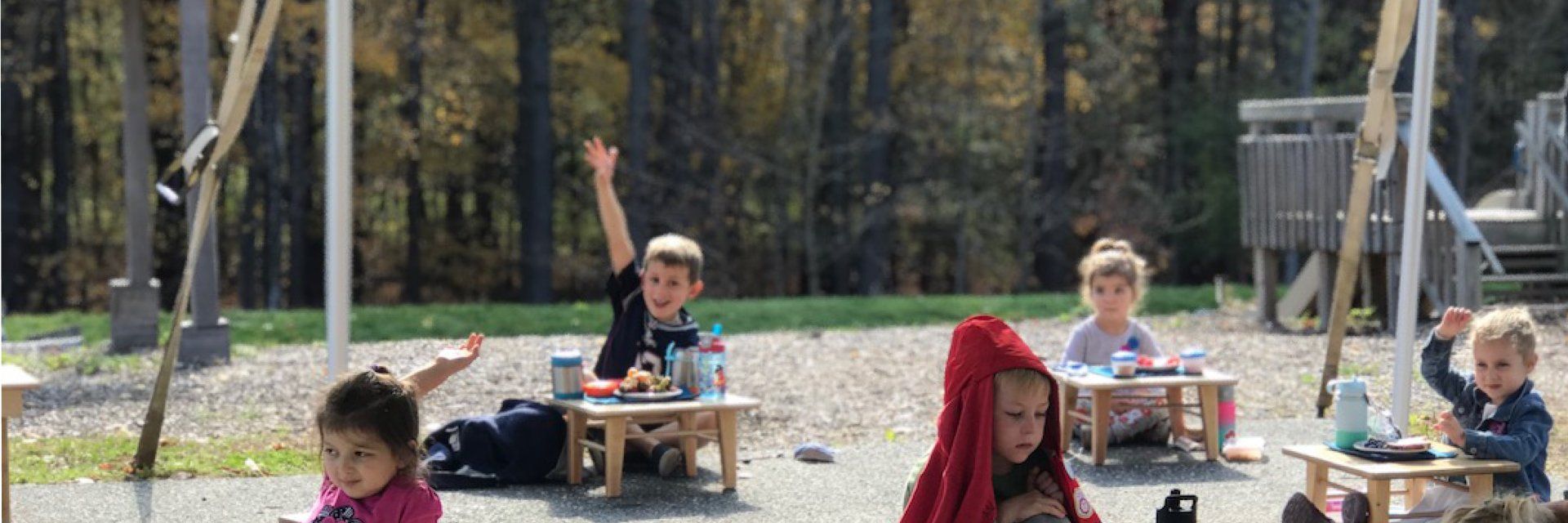 Preschool aged children eating lunch outdoors at individual tables