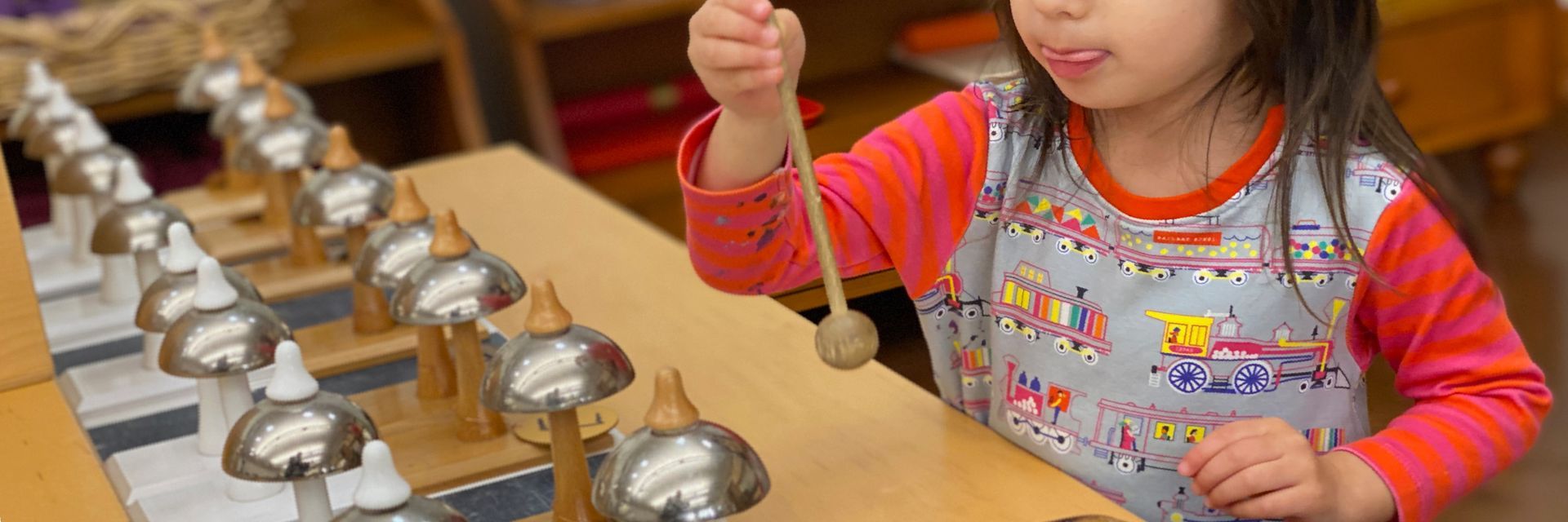 Image of a preschool child at standing at a table laid out with two rows of Montessori bells