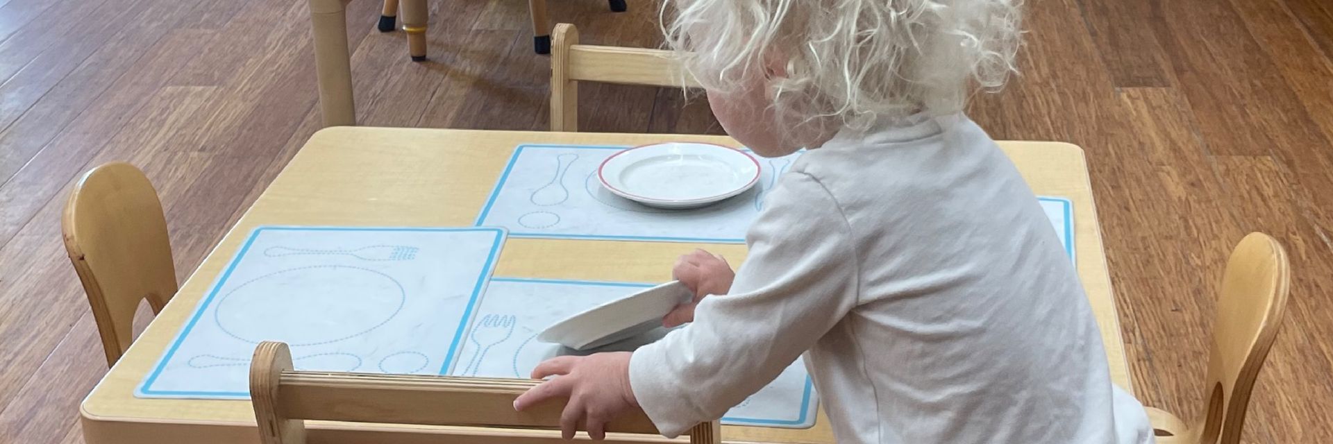 Image of a toddler aged child placing a plate onto a table using placemats with place setting diagrams