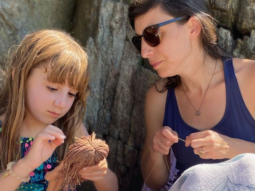Image of a woman and a girl sitting in front of a rock face working on crafts