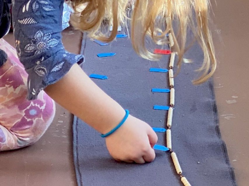 image of a preschool child kneeling on the floor over the 1000 bead chain