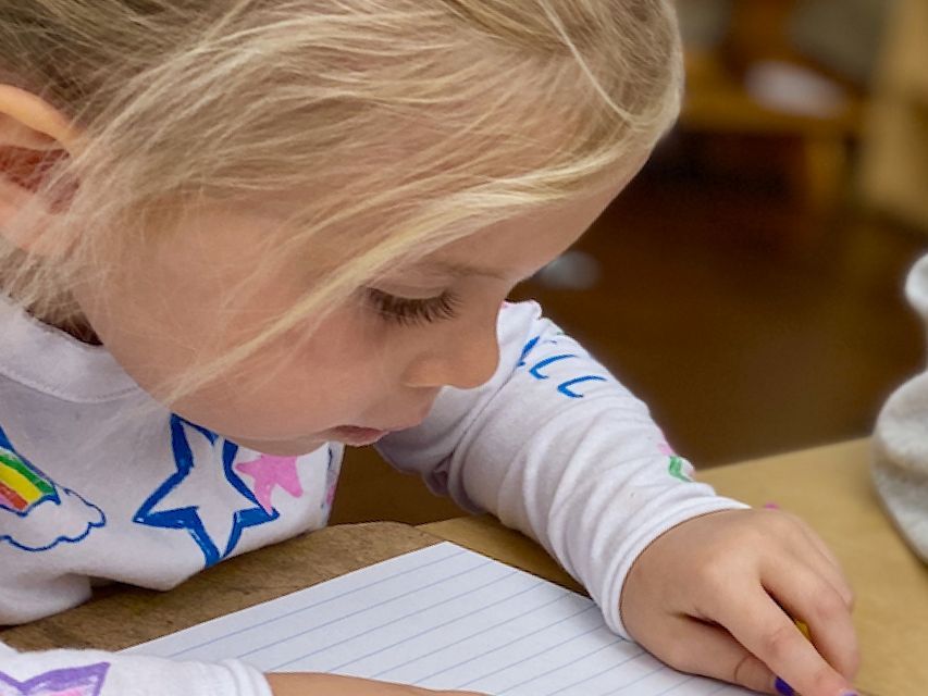 Image of a pre-school child sitting at a table looking intently at a piece of paper