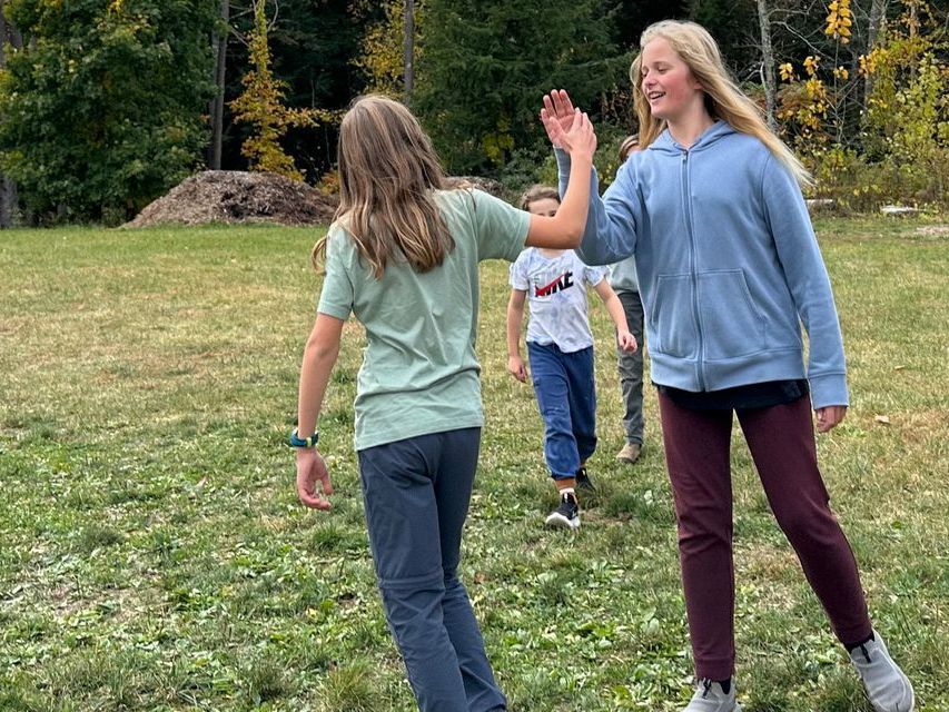 Image of two adolescent students outside on a field, giving each other a high five