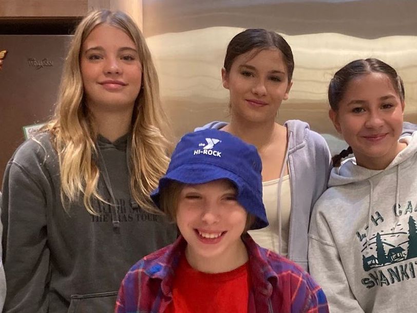 Image of four adolescent students of differing heights gathered smiling and standing together
