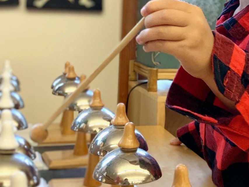 Image of a child's hand holding a small wooden mallet working with tone bells