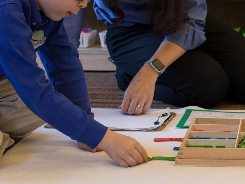 Elementary aged child working on a rug with colorful Montessori materials