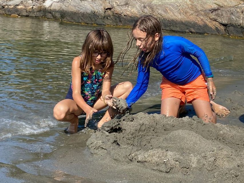 Image of two children kneeling in the sand by the water's edge