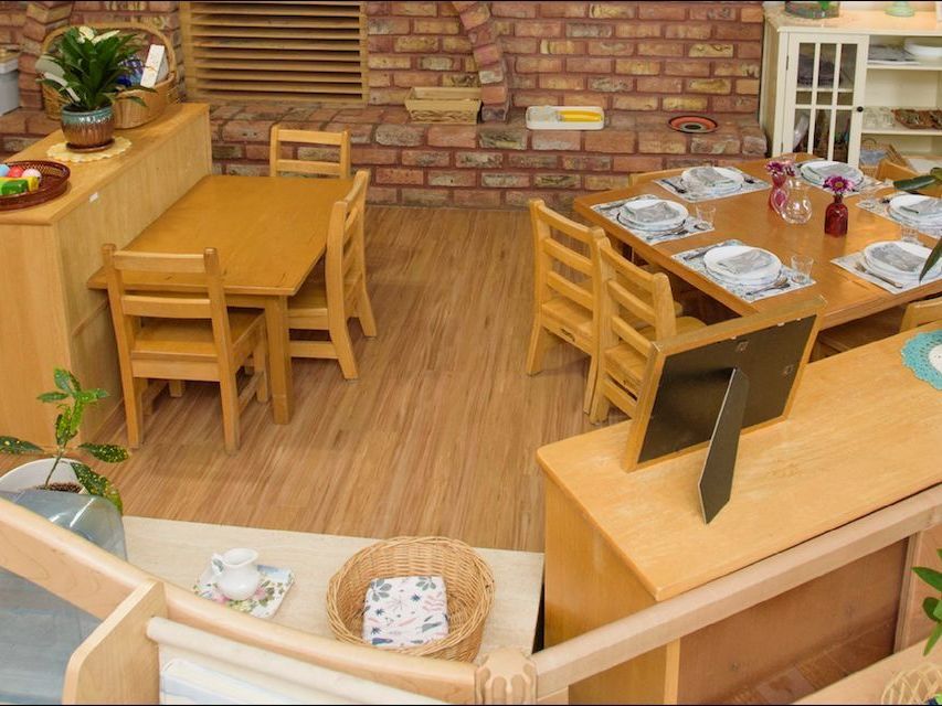 Image a toddler classroom with small tables and chairs, place settings, and low shelves