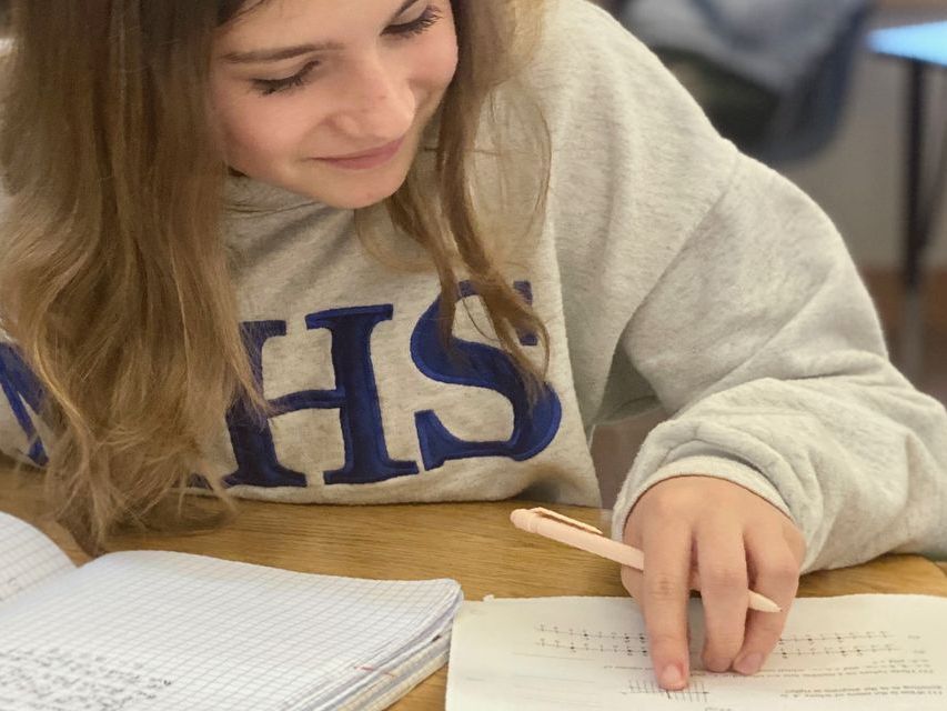 An adolescent student sitting at a table with a book and a notebook in front of her, reading