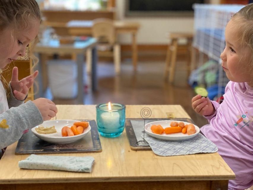 Image of two pre-school children at a small table set with china, silver ware, candle and place mats