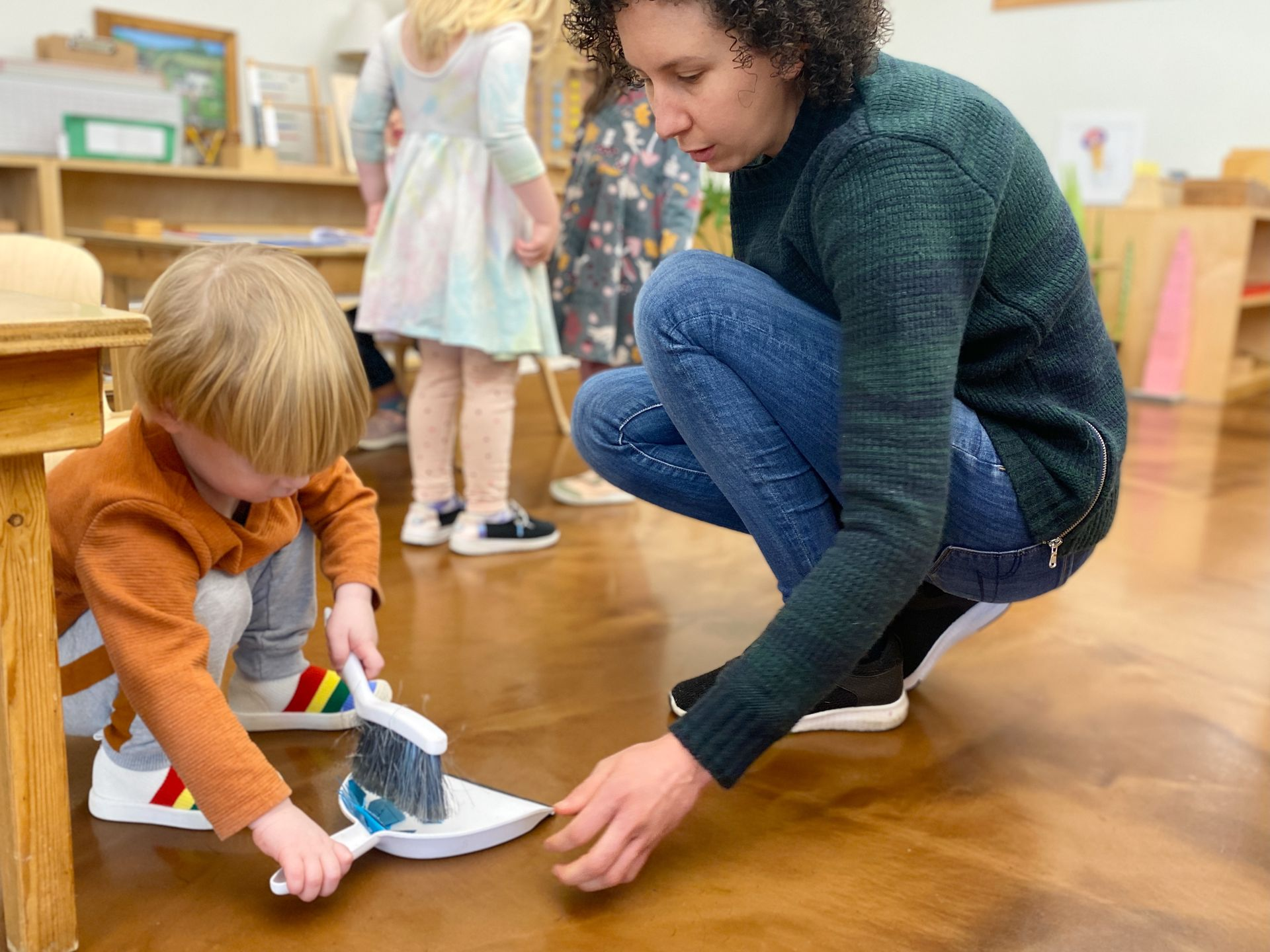 Image of a guide crouching near the floor with a child using a dustpan and brush 