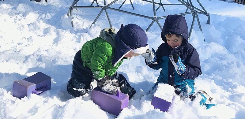 two preschool children playing in the snow making bricks
