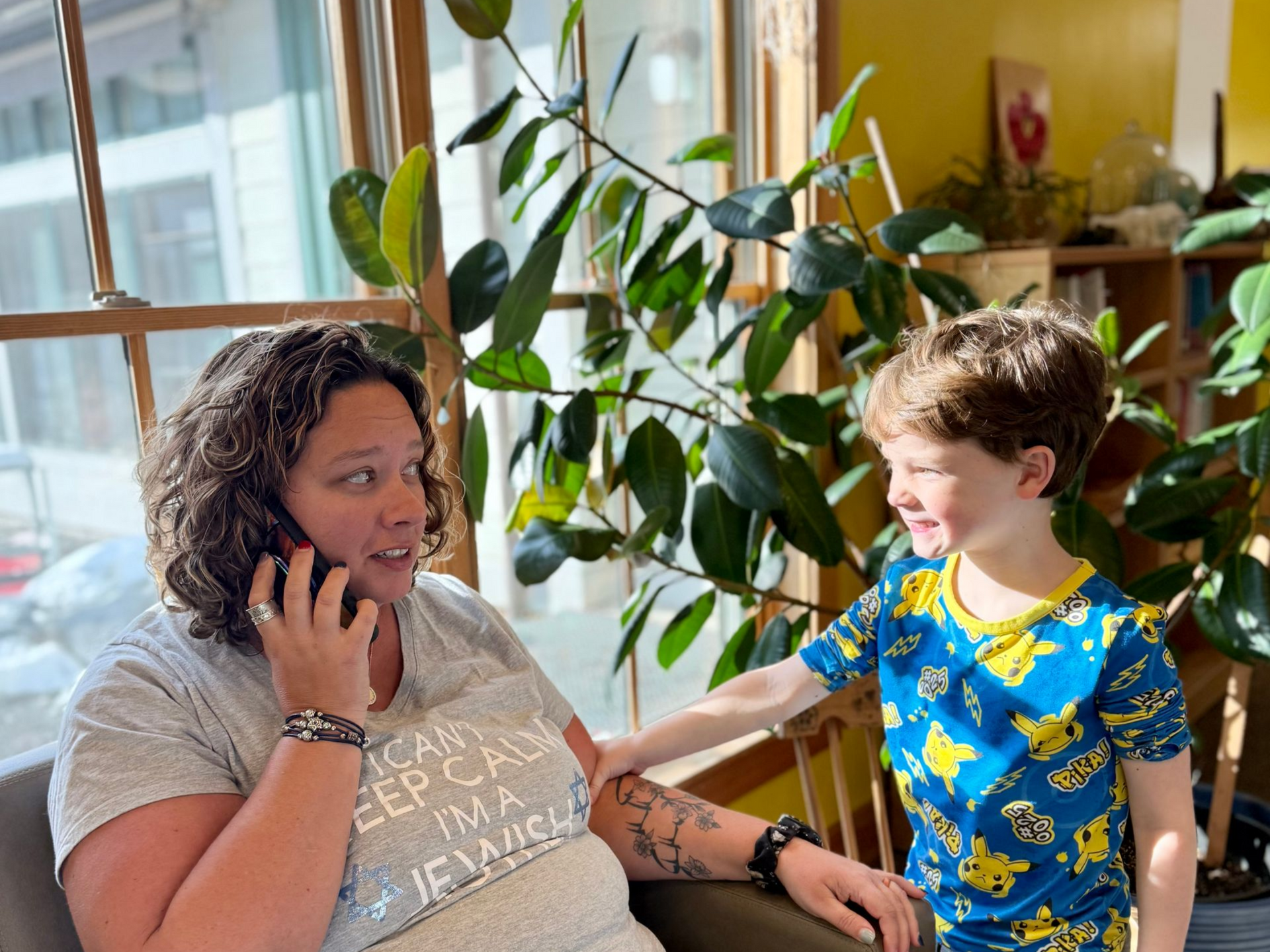image of an adult sitting on a couch talking on the phone with a child standing next to her