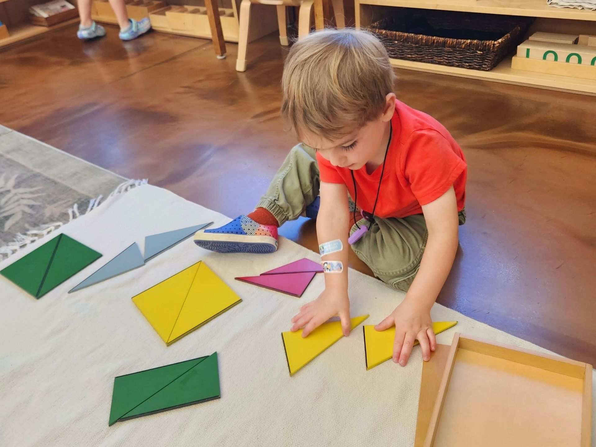 image of a preschool aged child sitting on a carpet with Montessori sensory materials, flat polygons