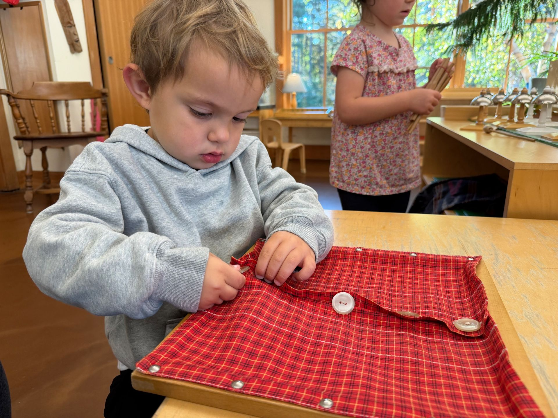 Image of a preschool child sitting at a small table with a fabric-covered wooden frame with buttons