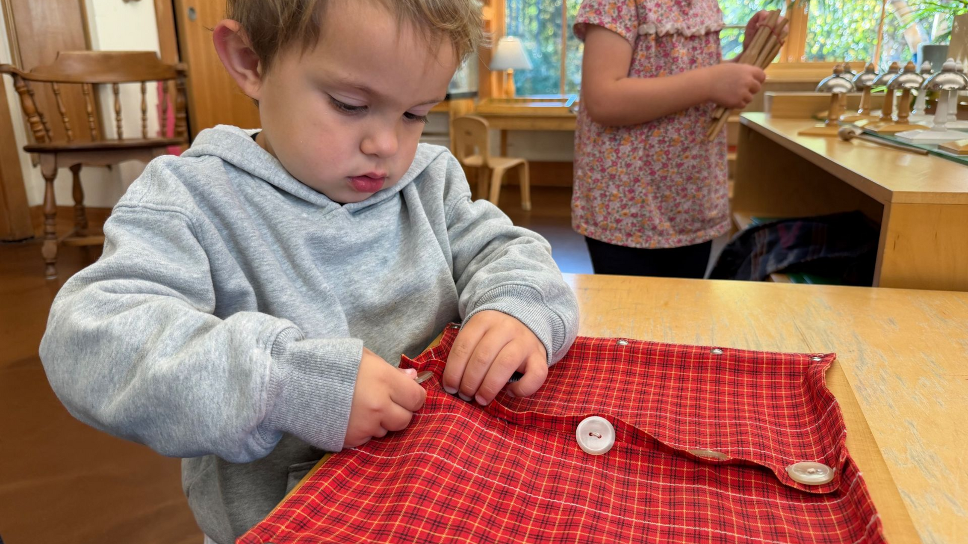 Image of a preschool aged child sitting at a small table with a wooden frame covered in fabric with large buttons