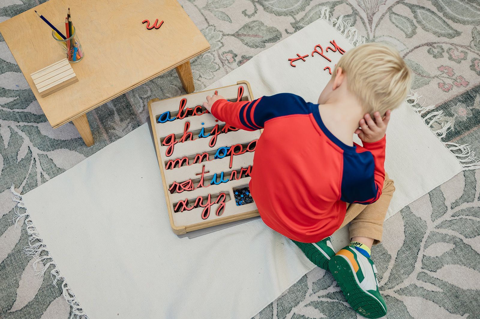 Image of a preschool aged student sitting on the floor with a moveable alphabet