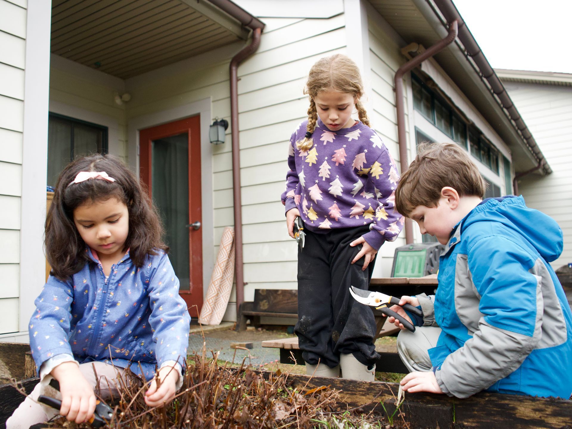 Image of three elementary students standing and crouching around a raised garden bed
