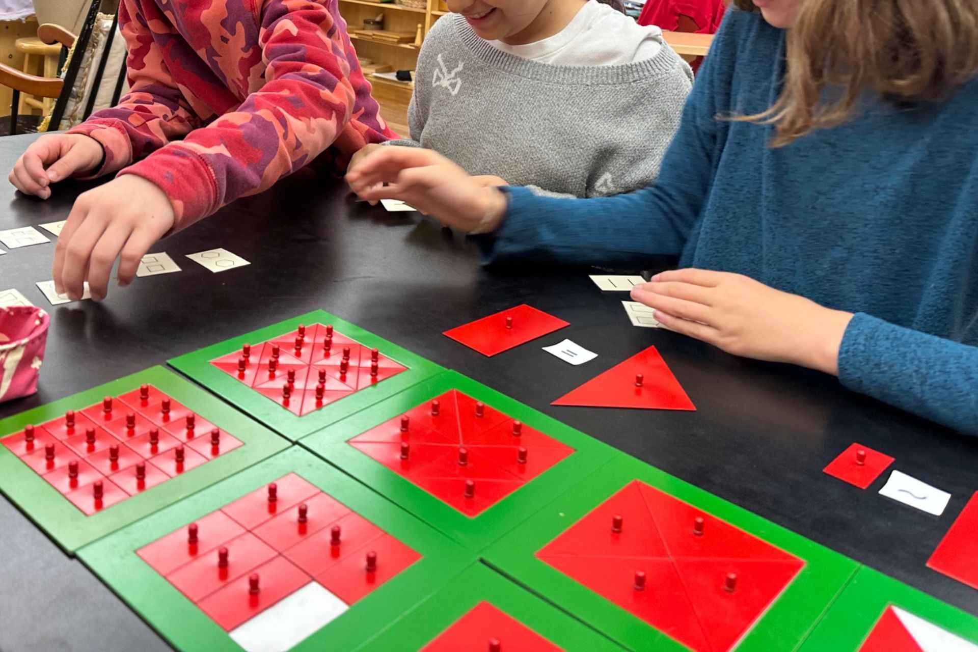 Image of three elementary students sitting at a table with red equivalence shapes set in green frame
