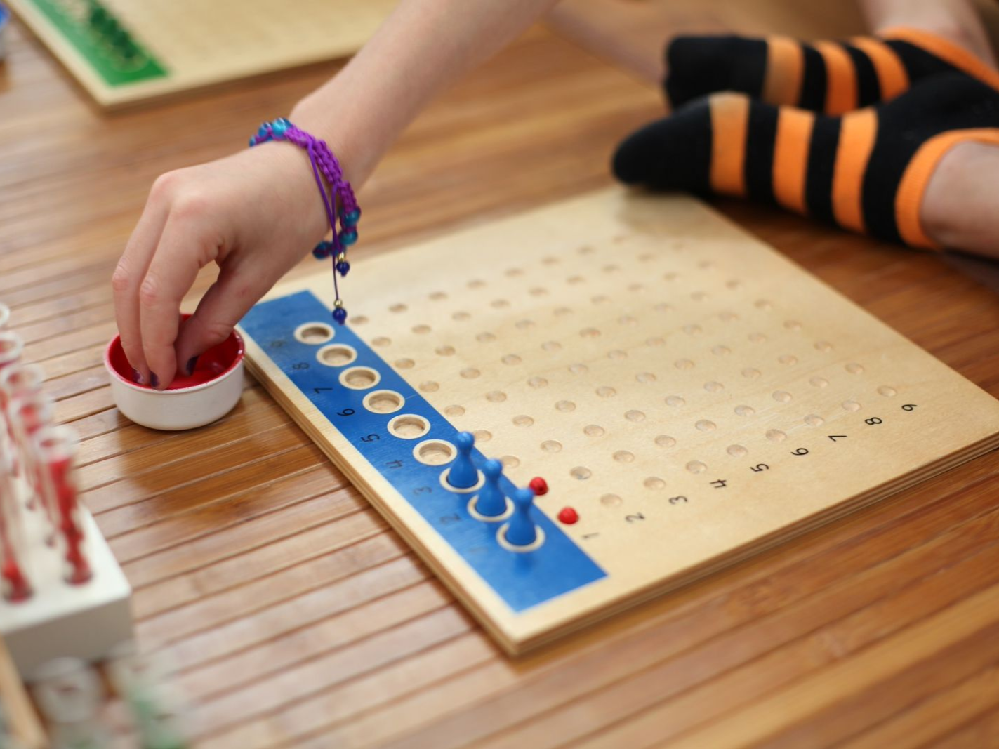 Close up of a rectangular board with 100 indentations in a 10 by 10 grid with beads and placeholders