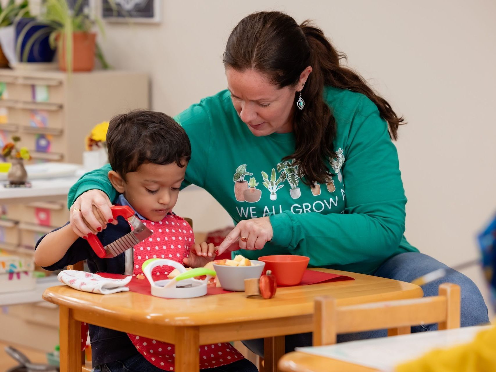 Image of an adult sitting next to a child at a small table, helpinga cooking task 