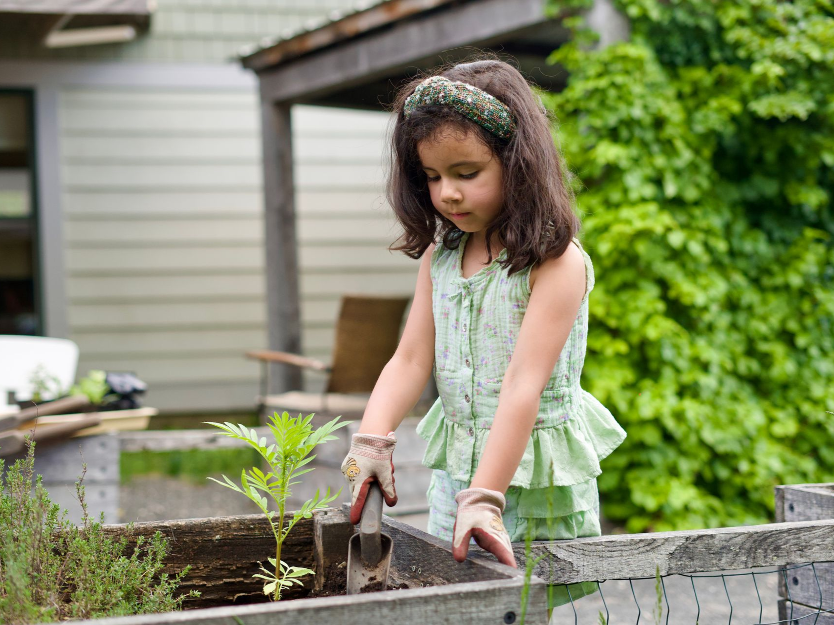 Image of an elementary girl standing with a trowel behind a raised garden bed