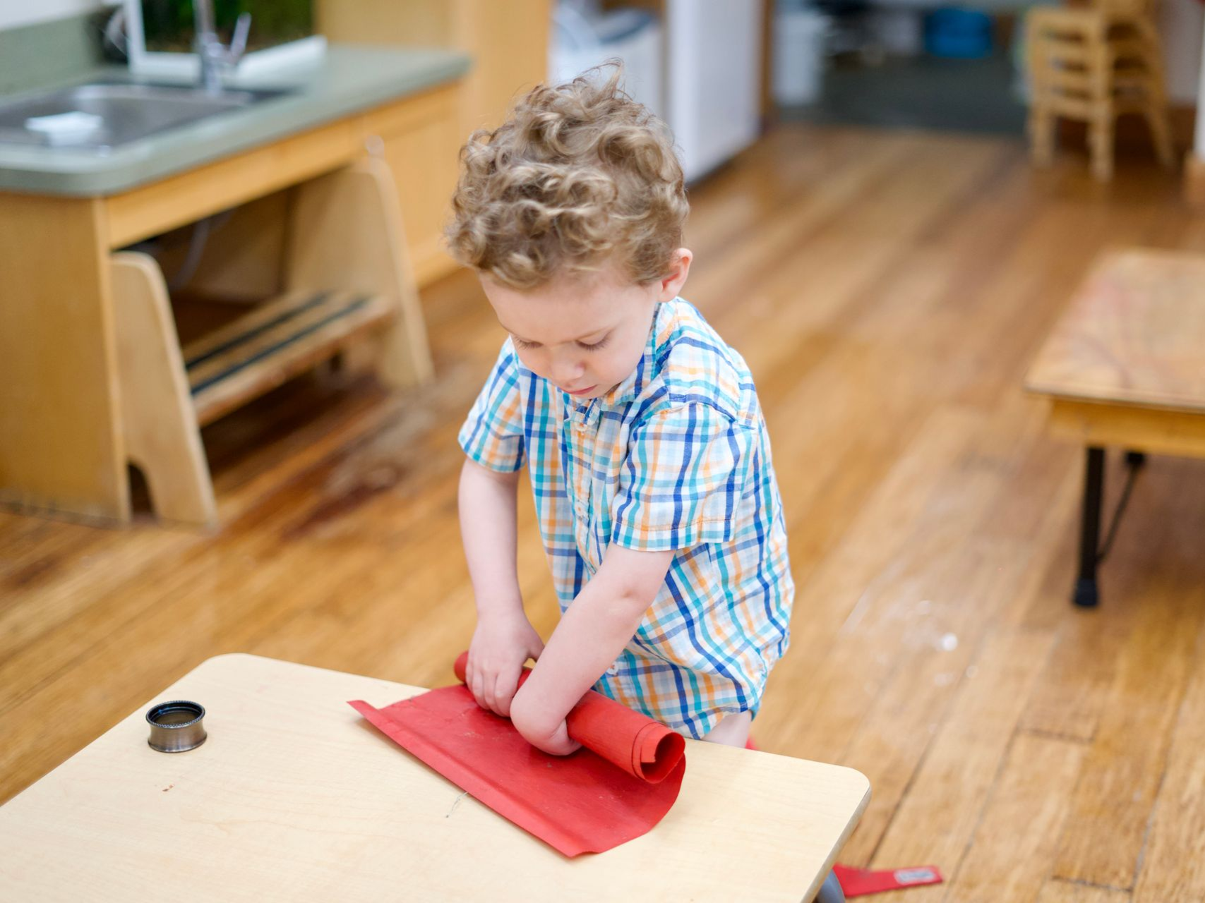 image of a preschool aged boy standing behind a low table rolling up a placemat