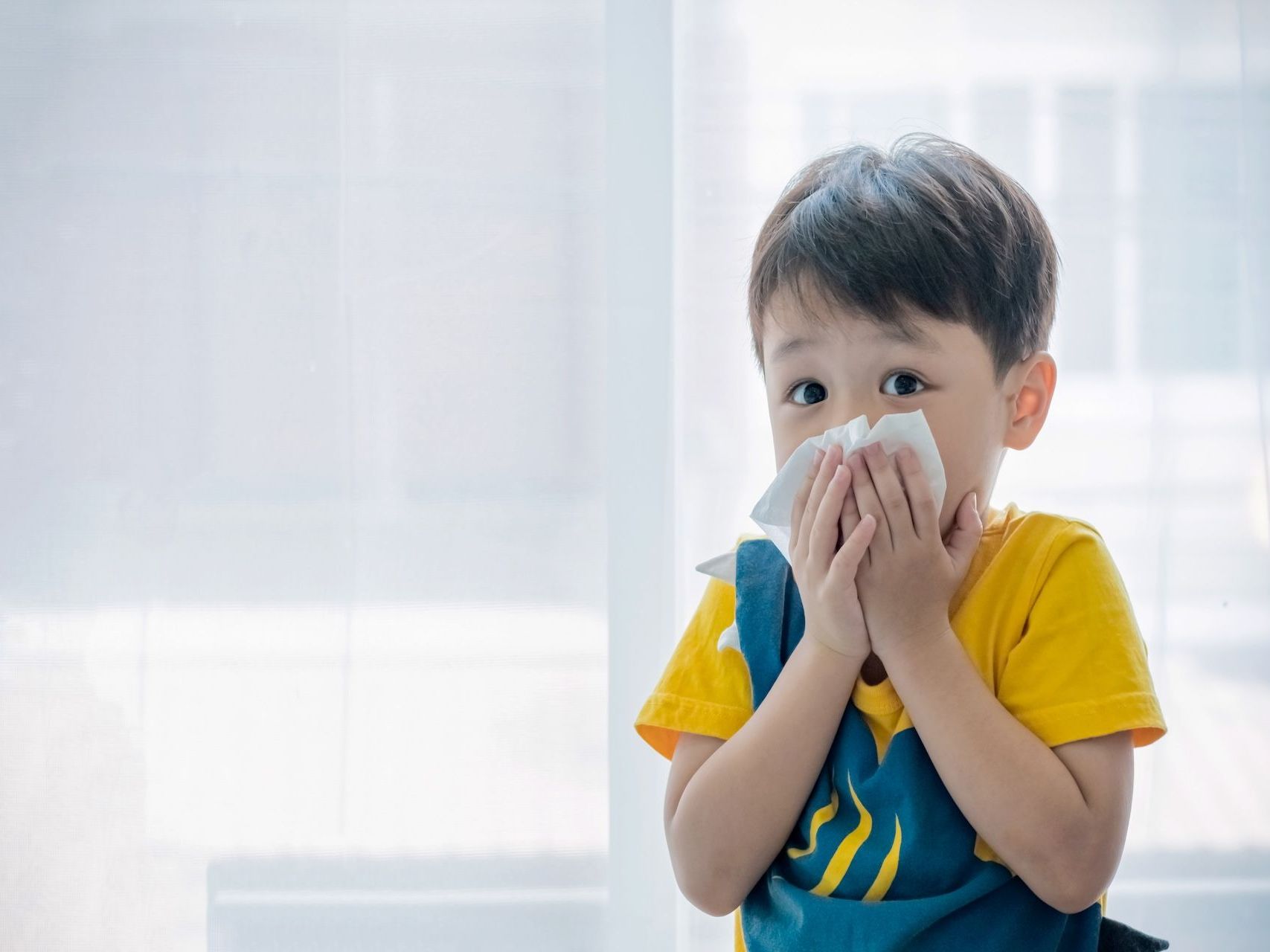 image of a preschool aged child holding a tissue to his noe while looking at the viewers