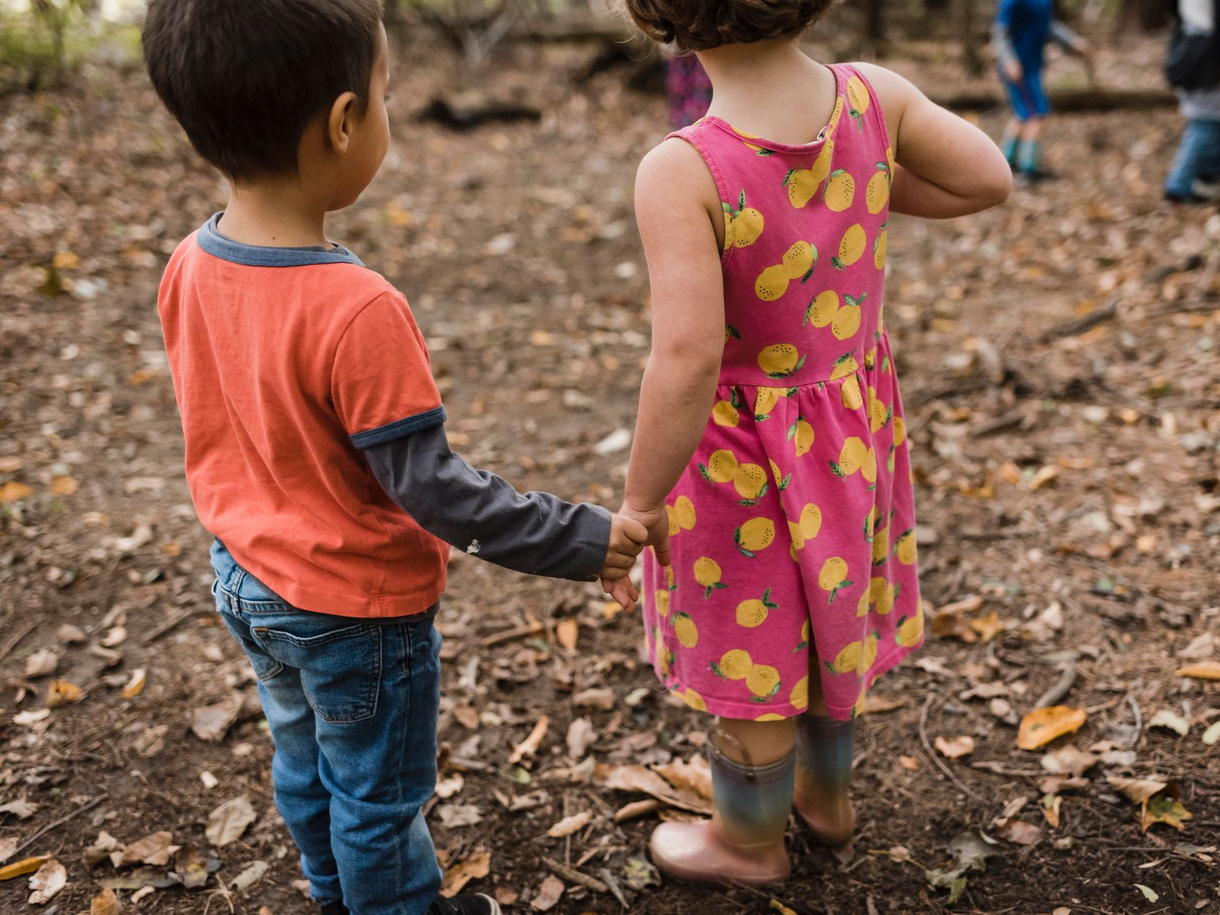 Image of two preschool children standing outdoors on woodchips, holding hands