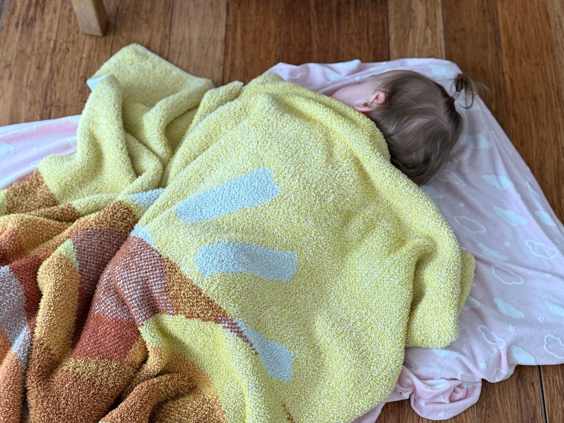 Image of a toddler sleeping face down on a mat with a brightly colored blanket
