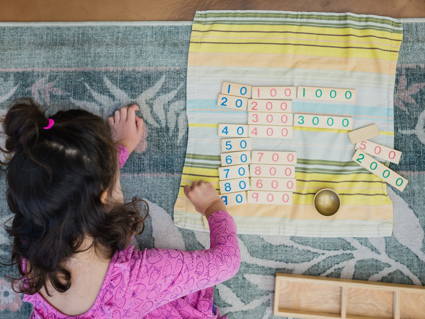 IImage of a preschool aged girl kneeling on a carpet working with tens, hundreds, and thousands