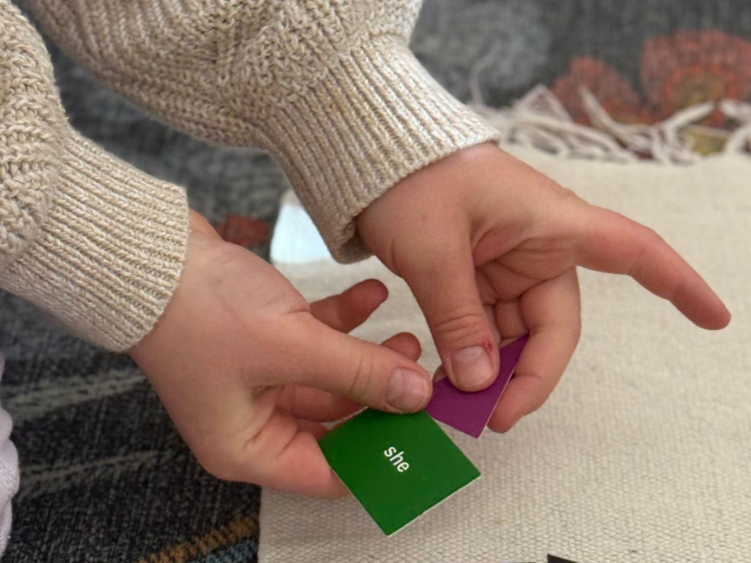 Close up image of a child's hands holding a small green square card printed with the word